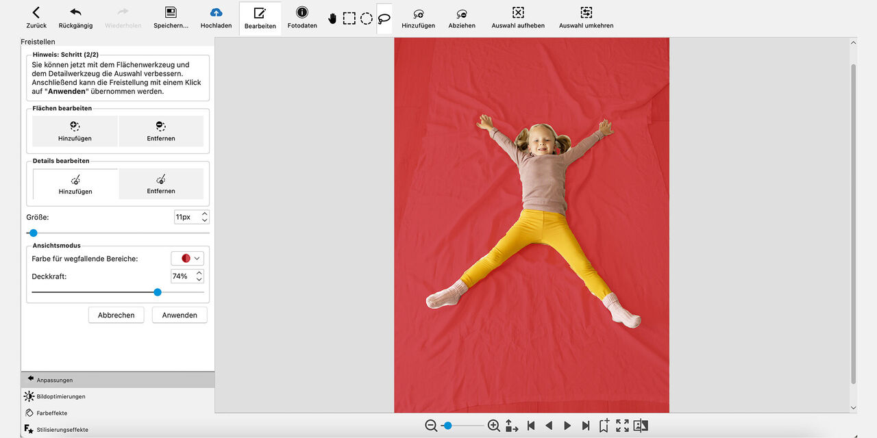 Snímek obrazovky z programu CEWE fotosvět: Dívka leží na zemi na rozprostřené dece a usmívá se do kamery. Má natažené obě ruce a nohy daleko od sebe. Pozadí, na kterém dívka leží, je zbarveno červeně.
